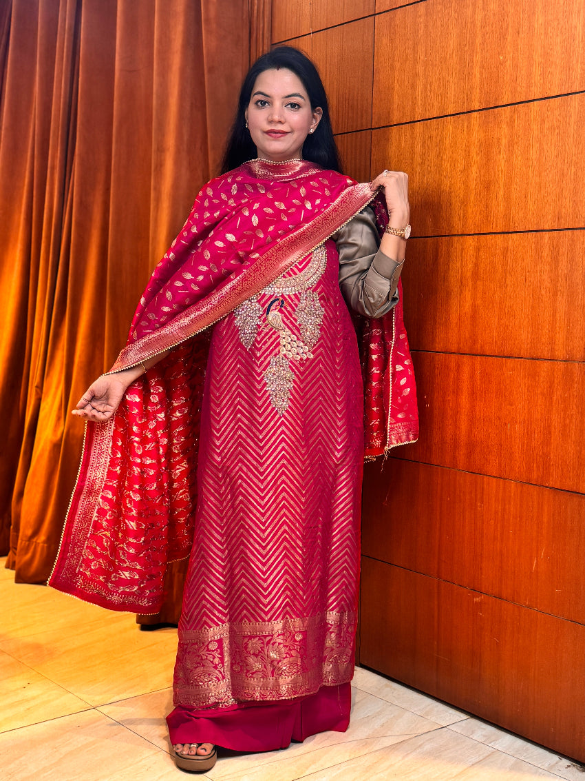 Woman wearing a traditional red and gold outfit with a matching shawl against a wooden wall.