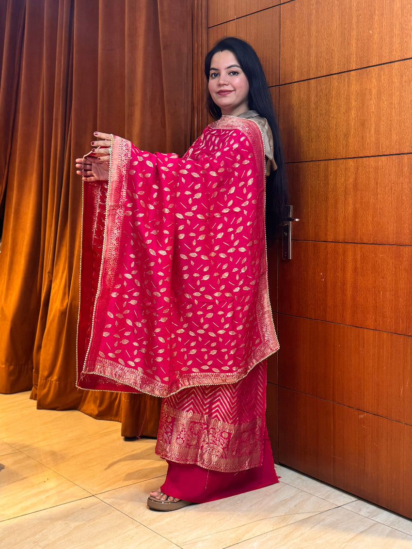 Woman holding a pink patterned dupatta against a wooden door.