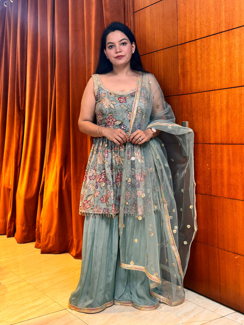 Woman in traditional outfit standing against a wooden paneled wall.