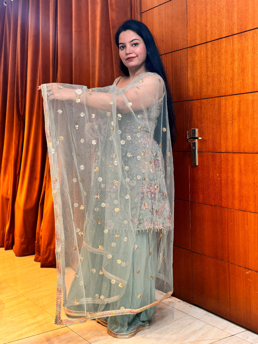 Woman holding a light blue embroidered dupatta against a wooden door background