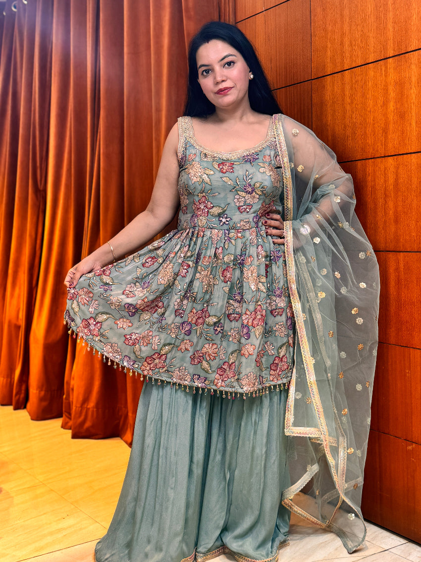 Woman in a floral traditional outfit standing against a wooden wall.