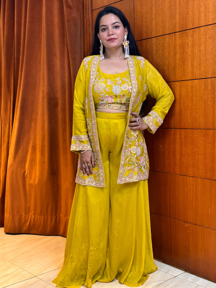 Woman in a yellow traditional outfit standing against a wooden paneled wall.