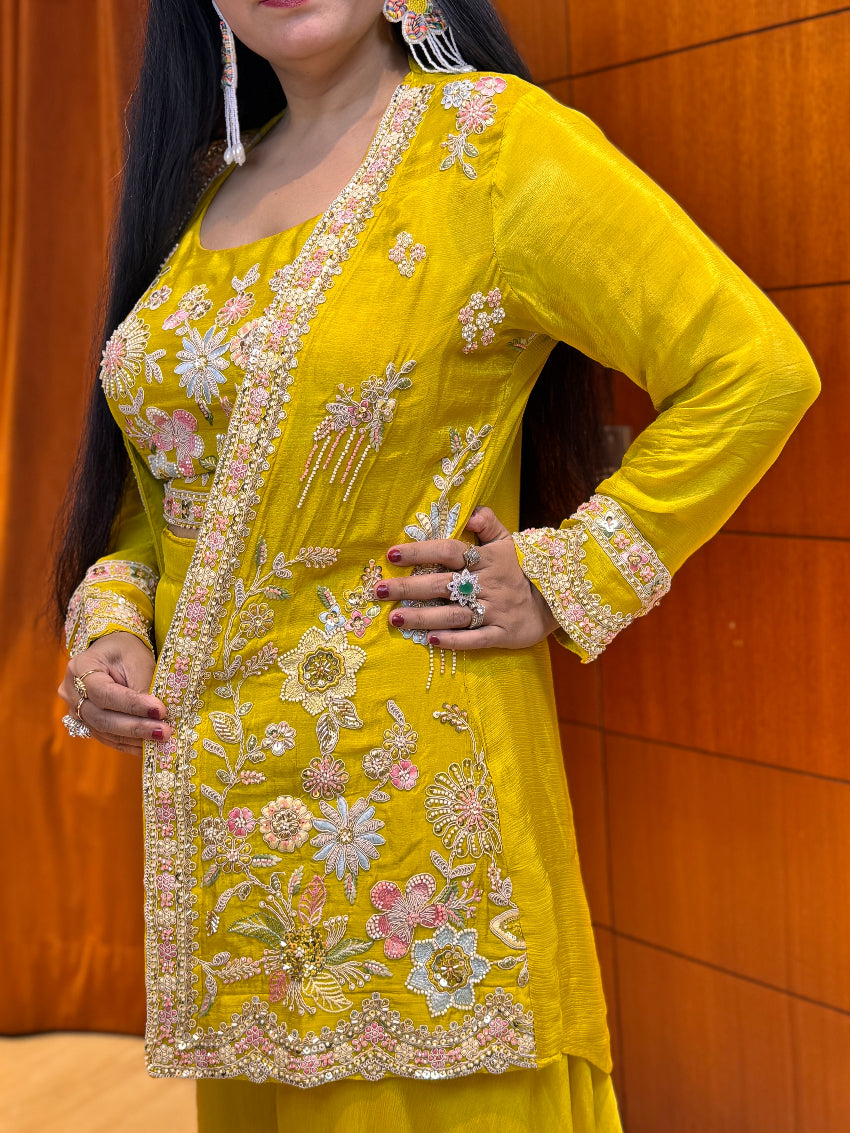 Woman wearing a yellow embroidered traditional outfit against an orange wall.