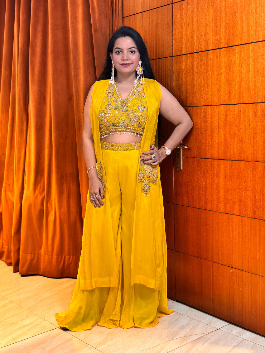 Woman in a yellow traditional outfit standing against an orange curtain.