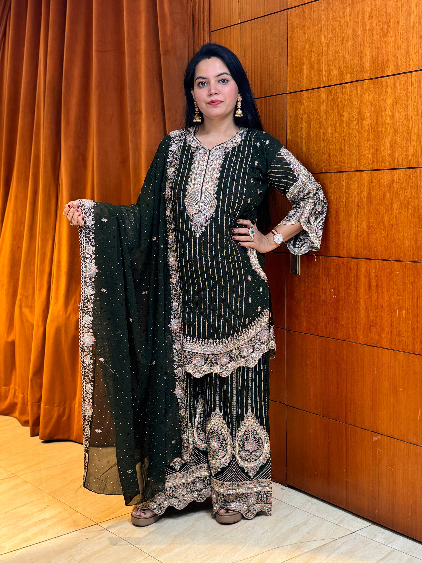 Woman in a black and gold traditional outfit standing against a wooden paneled wall.