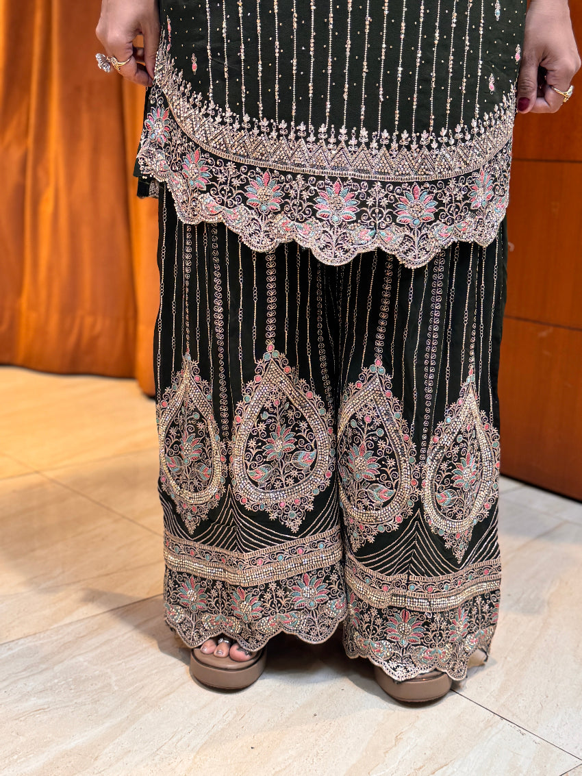 Black traditional outfit with intricate white embroidery on a wooden floor.