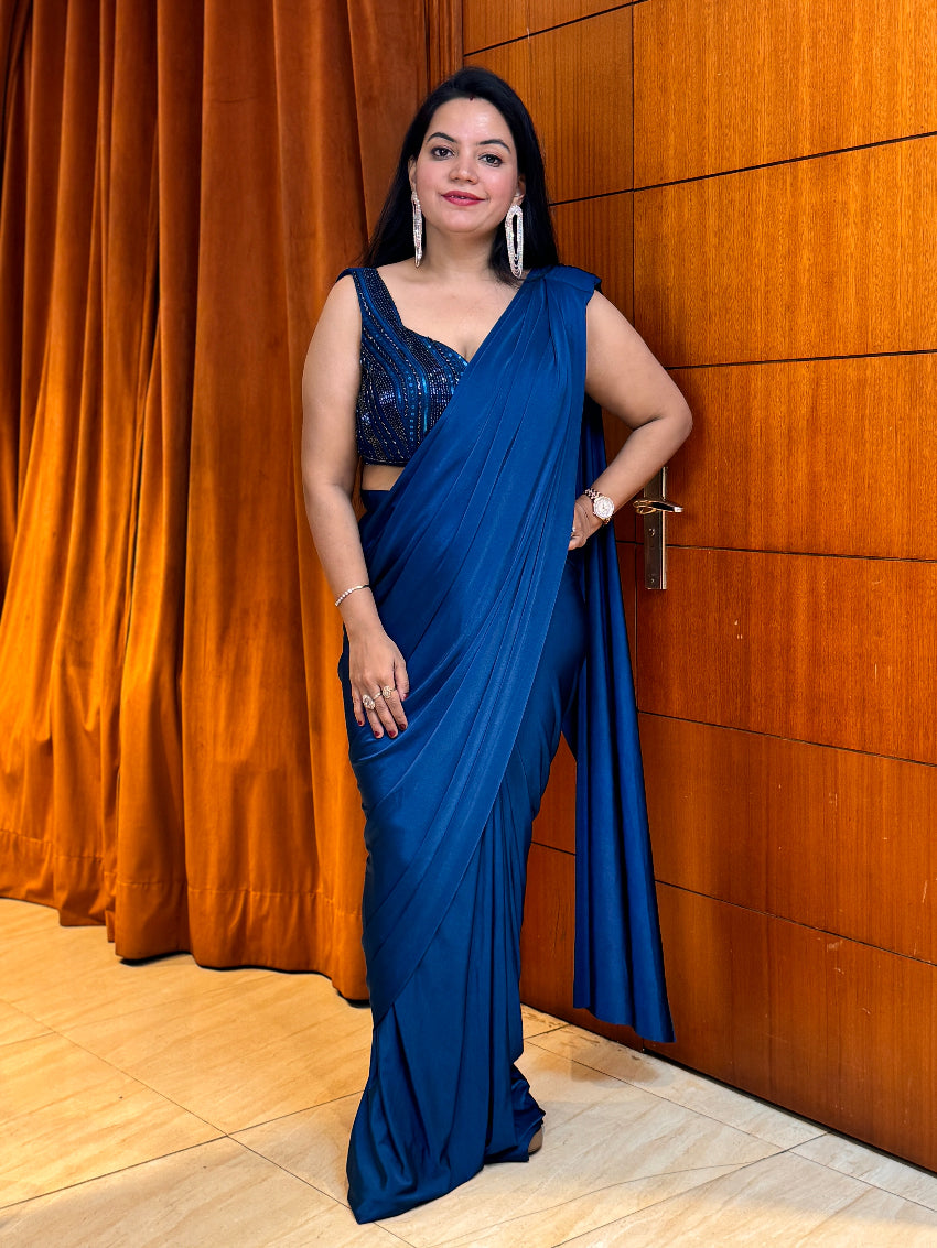 Woman in a blue saree standing against a wooden wall.