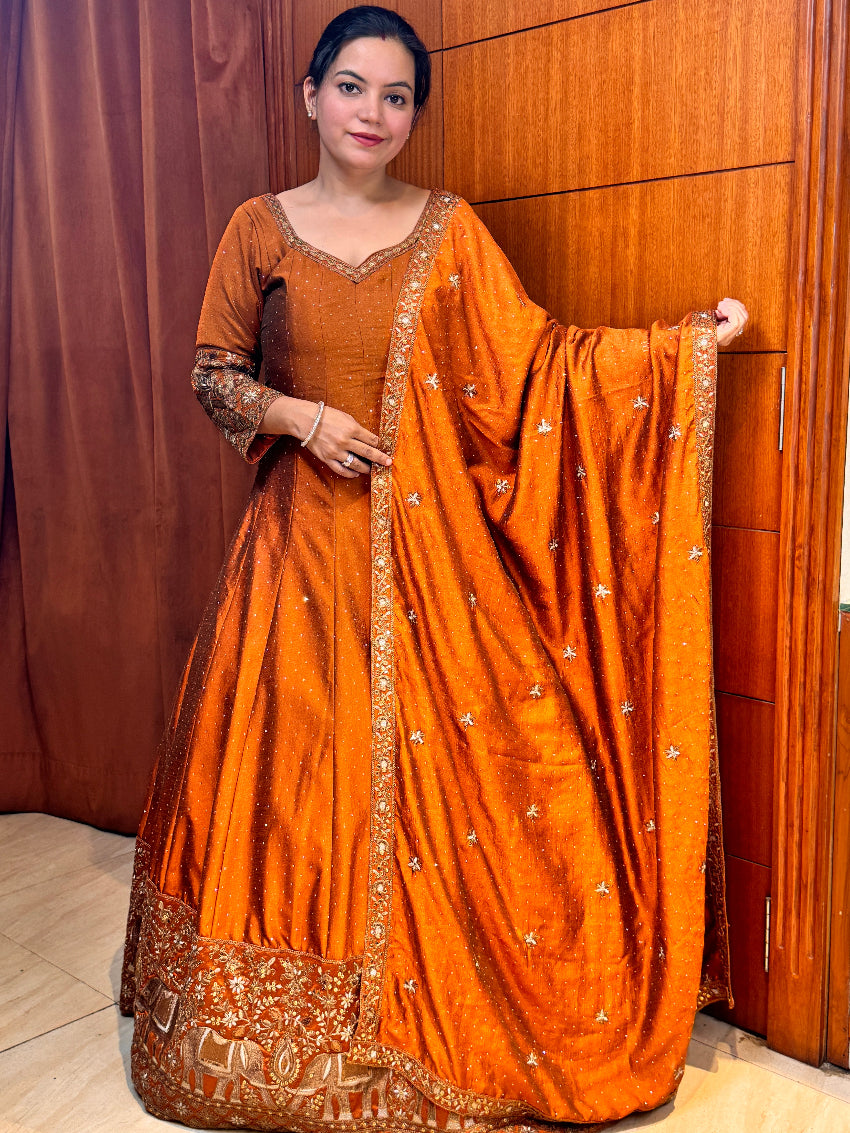 Woman wearing an orange saree with gold border in a room.