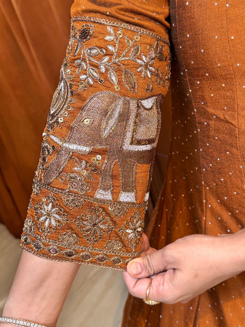 Close-up of a hand holding an intricately embroidered brown fabric with floral patterns.