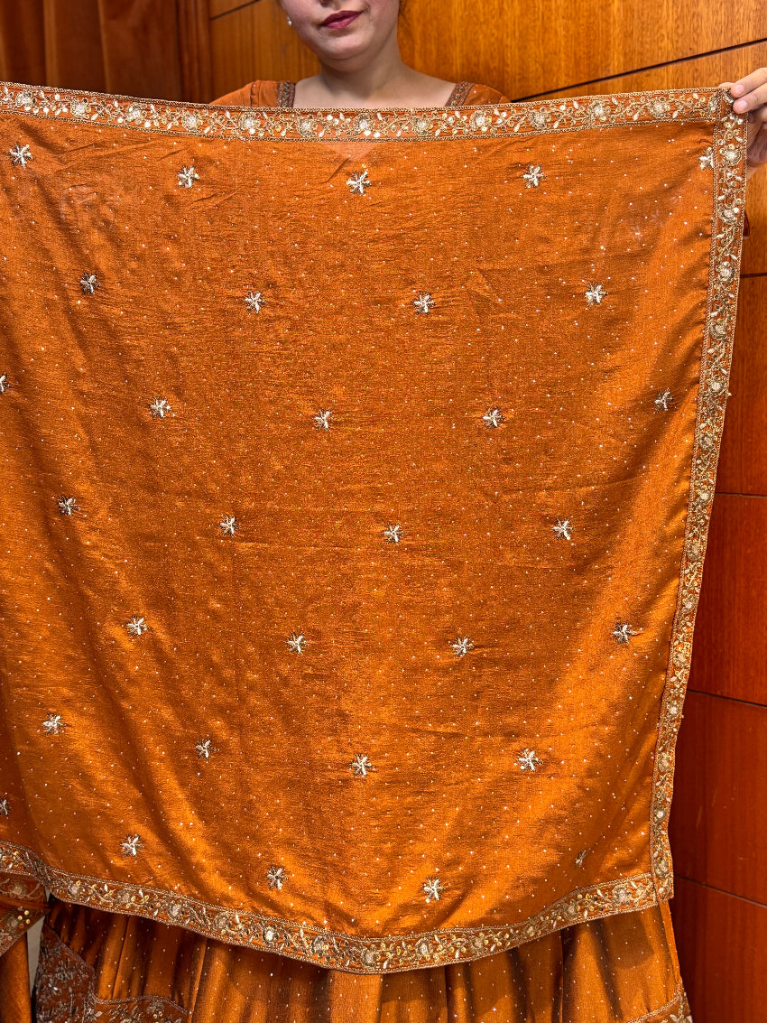 Orange fabric with silver embellishments held by a person against a wooden background