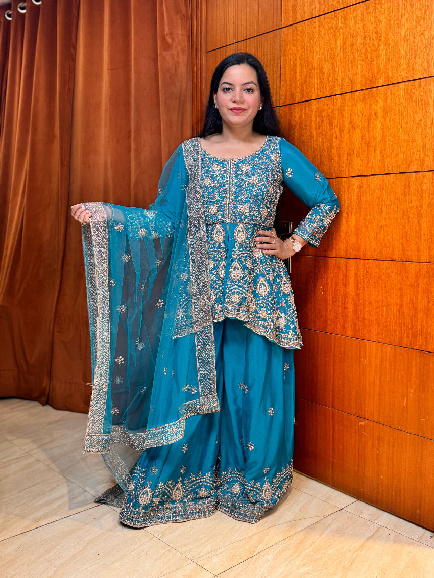 Woman in a blue embroidered traditional outfit standing against a wooden wall.