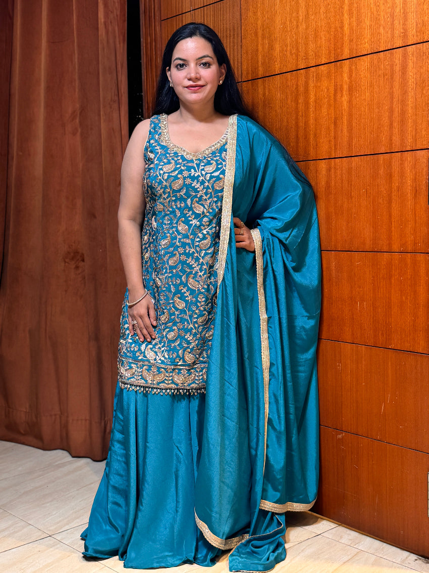 Woman in a blue traditional outfit standing against a wooden wall.