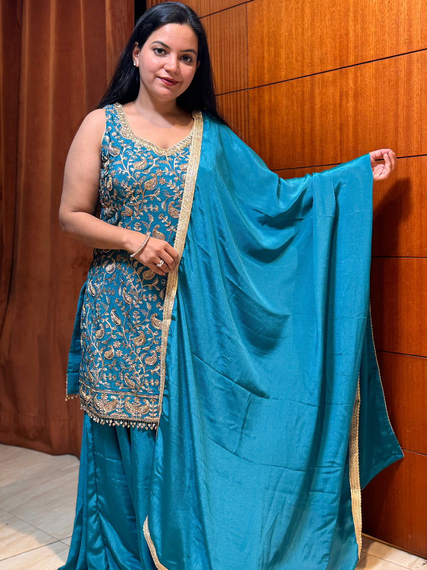 Woman wearing a blue traditional outfit with a matching dupatta against a wooden panel background