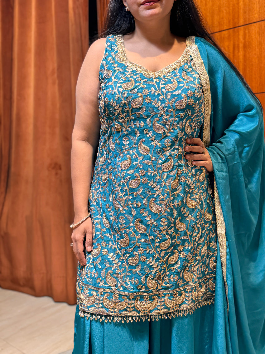 Woman wearing a blue embroidered traditional outfit with a plain background