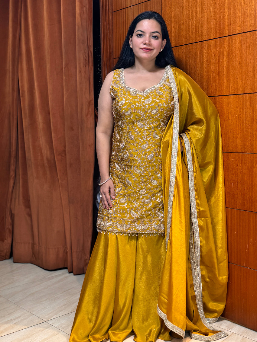 Woman in a yellow traditional outfit standing against a wooden wall.