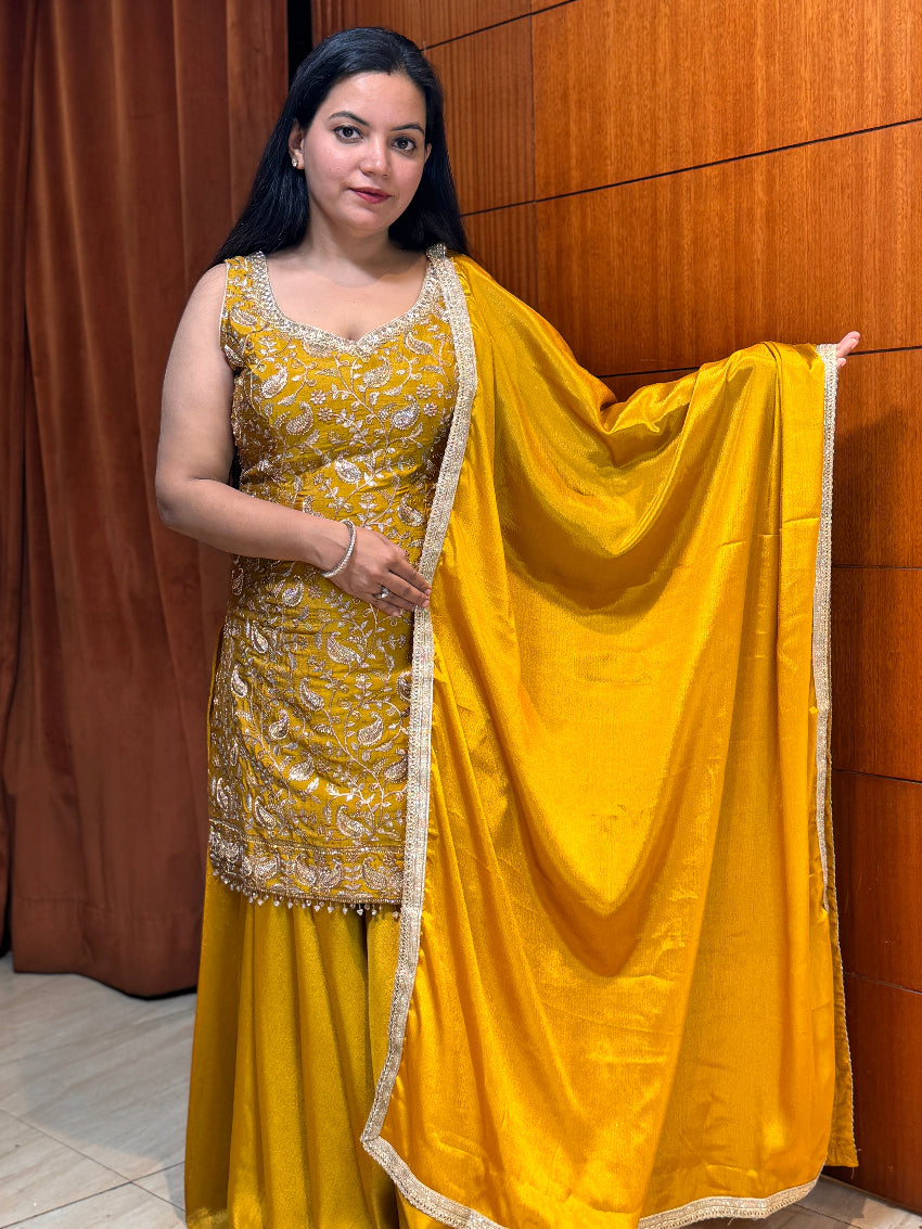 Woman in a yellow traditional outfit with a matching dupatta against a wooden panel background