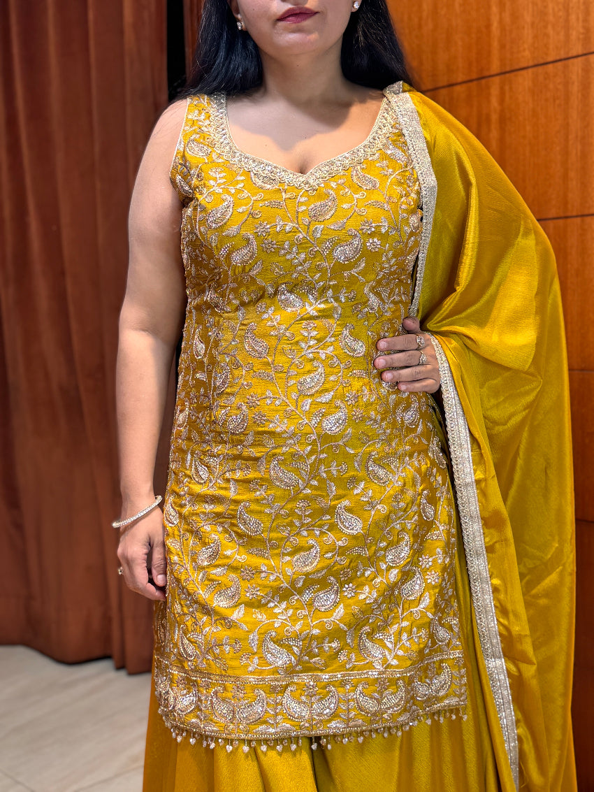 Woman wearing a yellow embroidered traditional outfit with a matching dupatta against a brown background