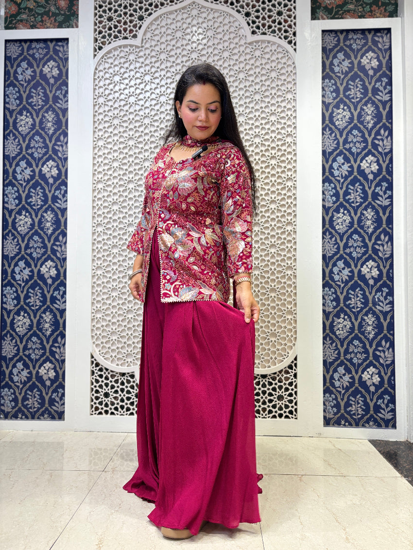 Woman in a floral top and pink skirt standing in front of a decorative wall.