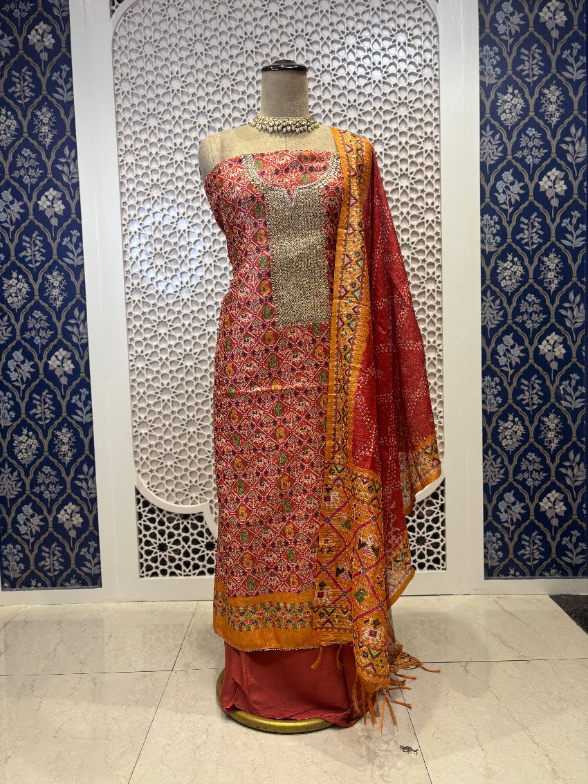 Traditional outfit with embroidered top and red dupatta on a mannequin against a decorative wall.
