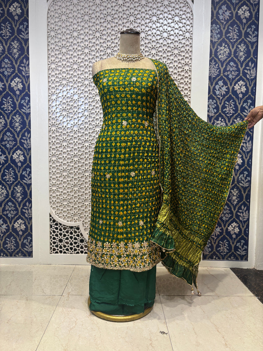 Green and gold traditional outfit with a dupatta on a mannequin against a decorative wall.
