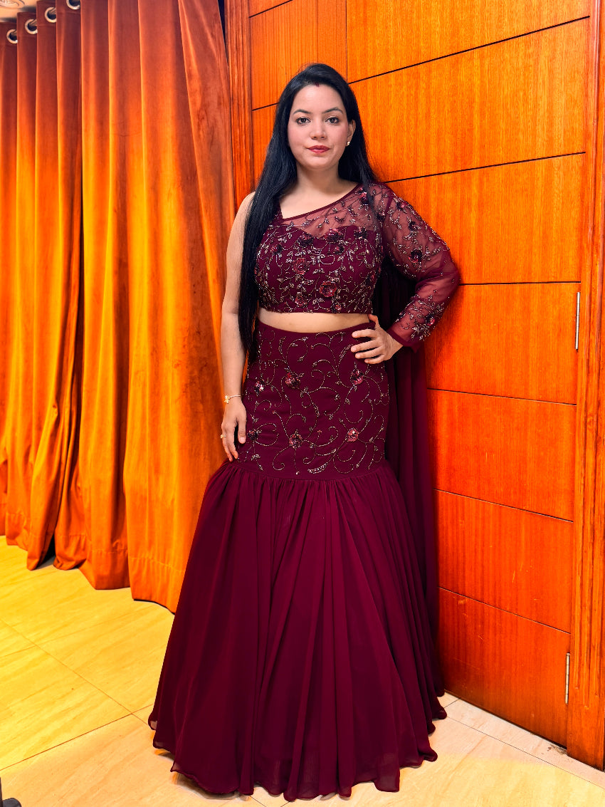 Woman in a burgundy traditional outfit standing against an orange curtain.