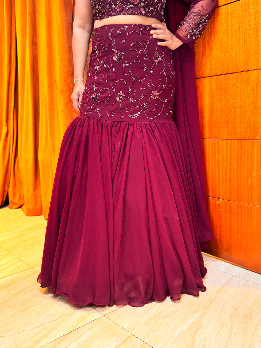Maroon traditional outfit with intricate design against an orange curtain background