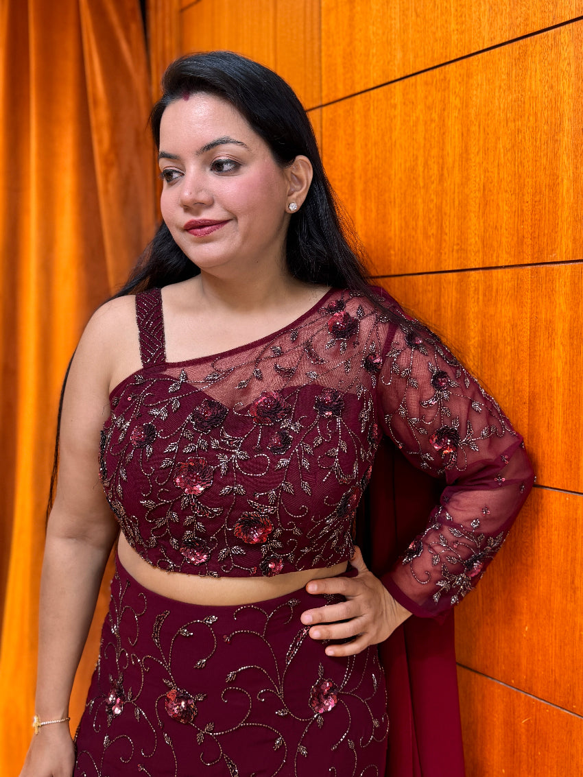 Woman wearing a maroon embroidered traditional outfit against an orange curtain.