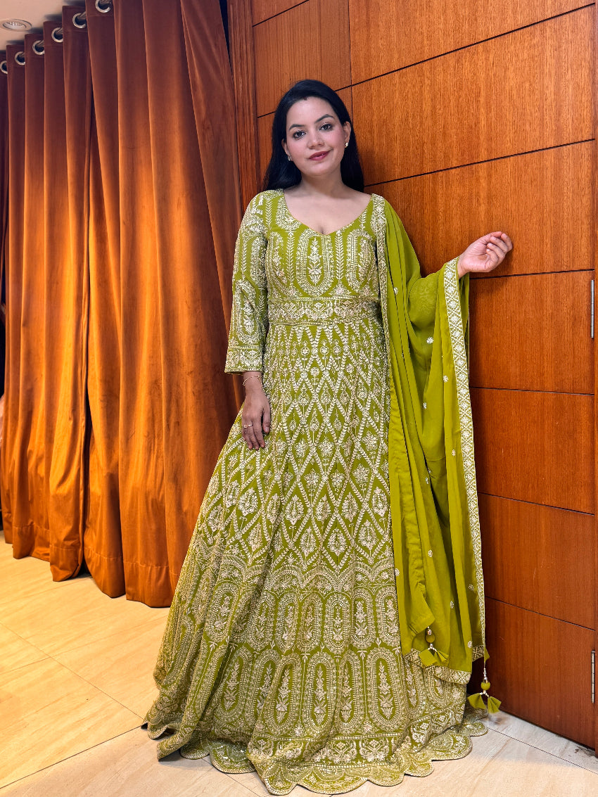 Woman in a green and white patterned traditional outfit standing against a wooden panel wall.