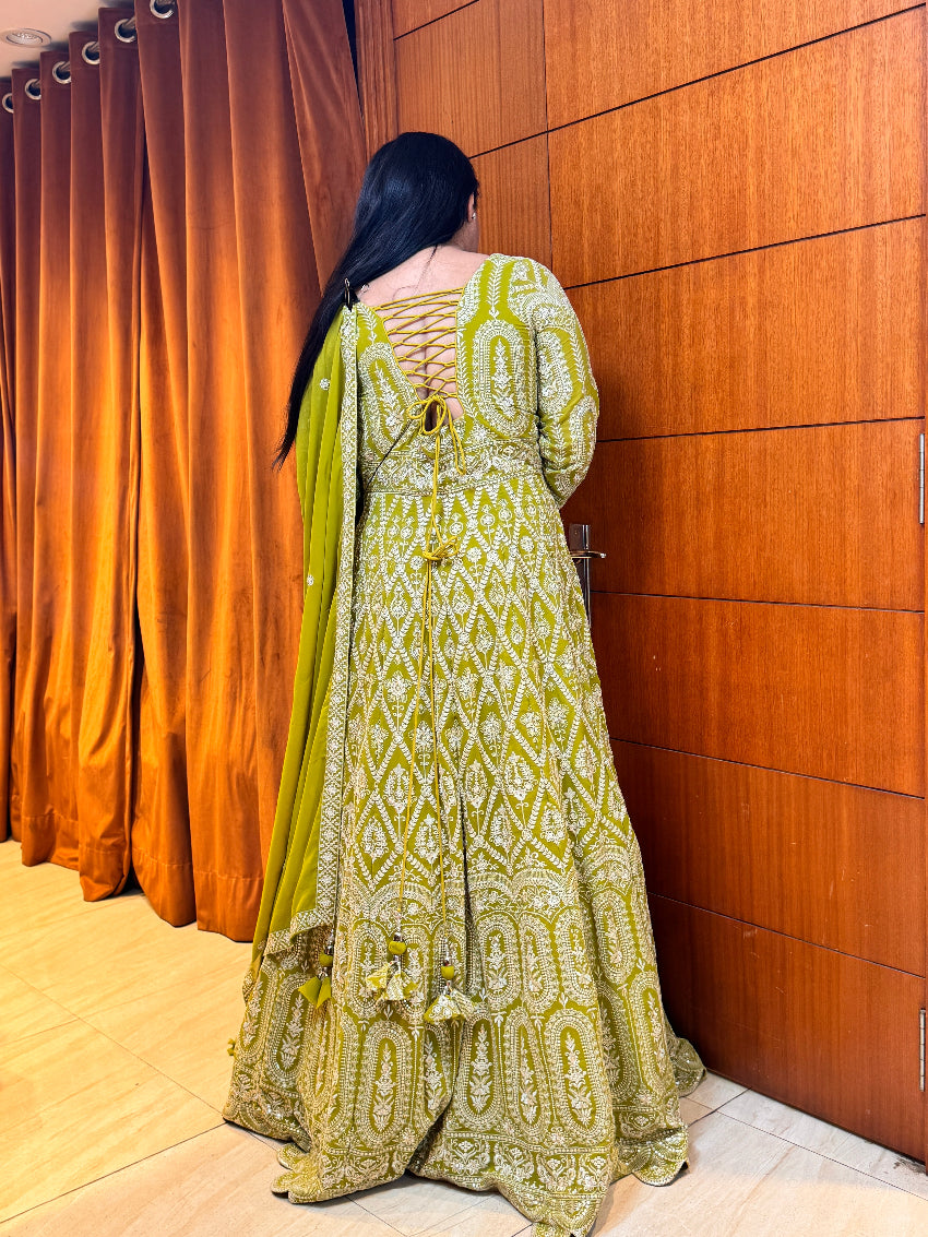 Woman in a green and white patterned dress standing against a wooden panel wall.
