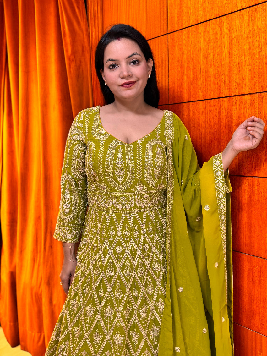 Woman wearing a green traditional outfit with white patterns against an orange curtain.