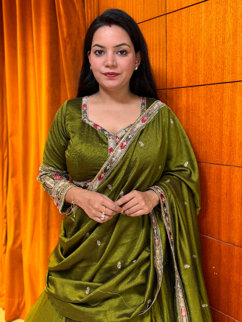 Woman wearing a green saree with a floral blouse against an orange curtain background