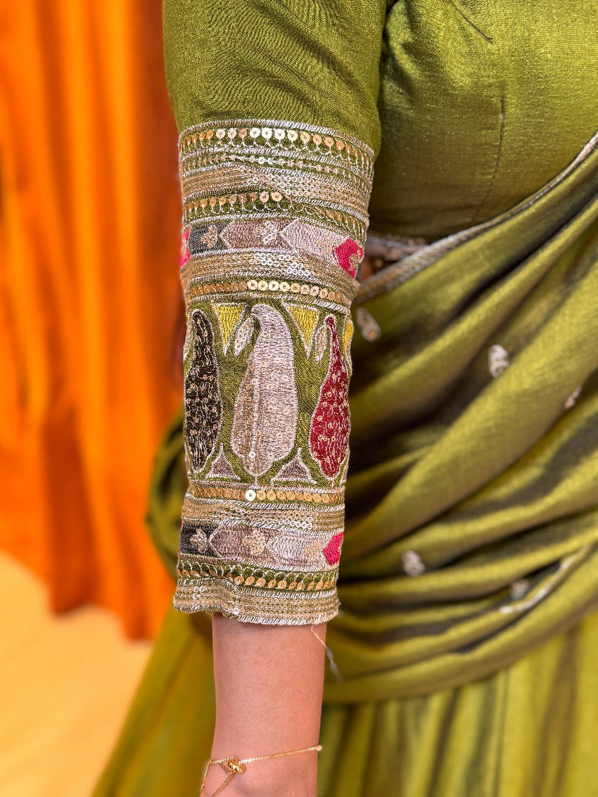 Green saree with intricate gold and silver embroidery on a blurred orange background