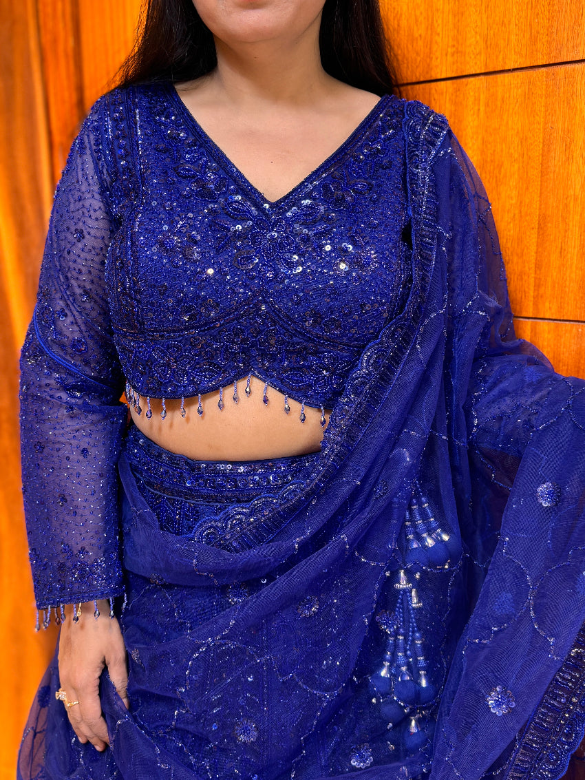 Person wearing a blue embroidered saree with a matching blouse against a wooden background