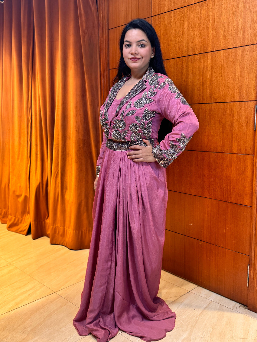 Woman in a pink traditional outfit standing against a wooden paneled wall.