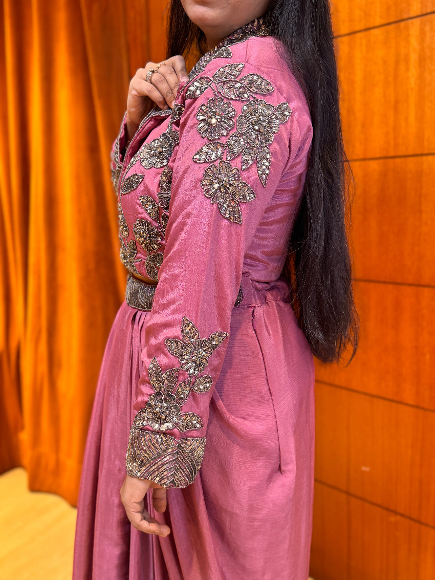 Person wearing a pink outfit with silver embellishments against an orange curtain background