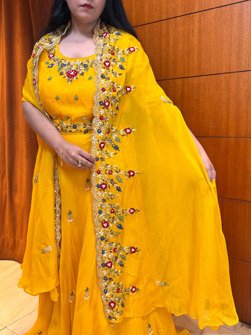 Person wearing a yellow traditional outfit with intricate embroidery against a wooden panel background