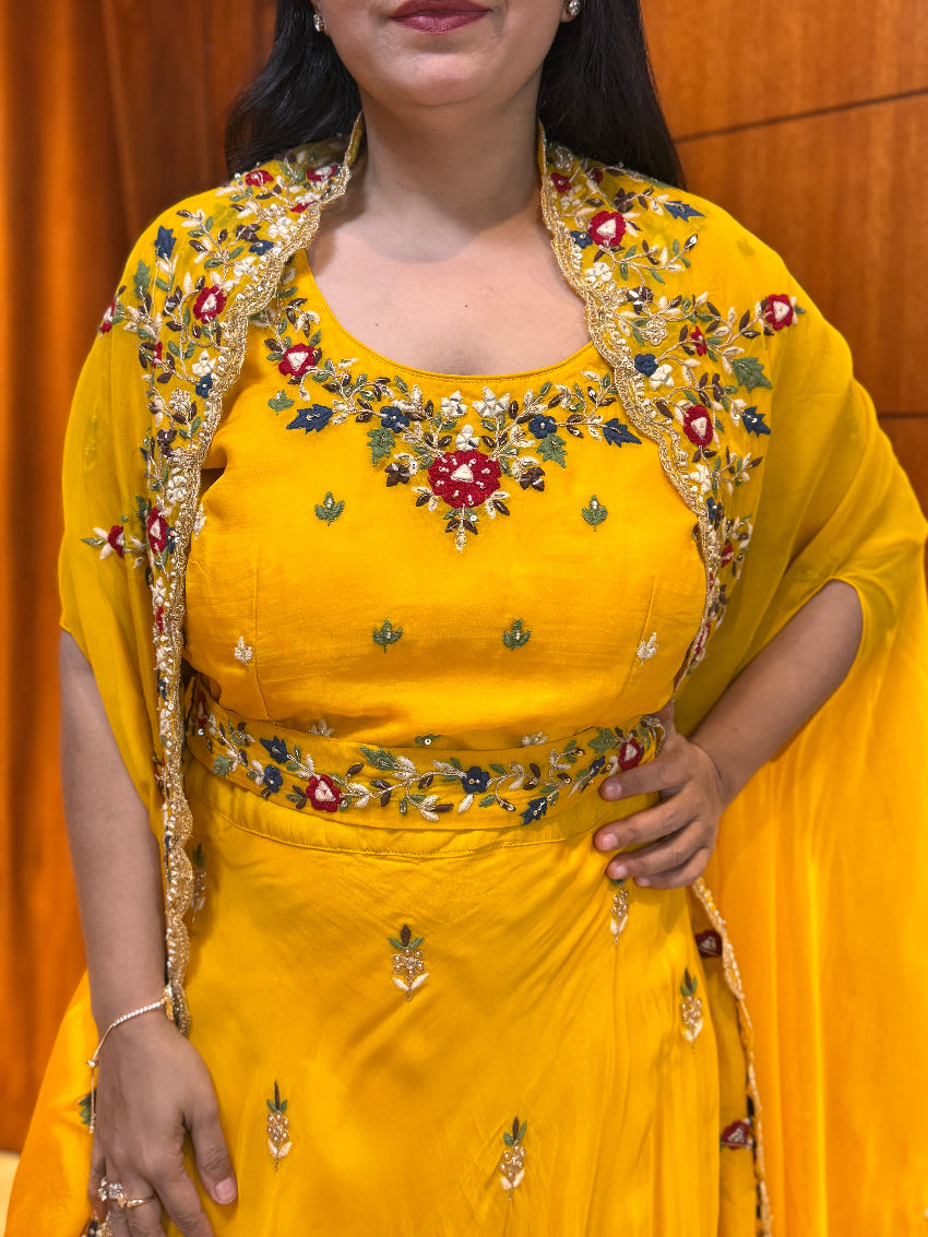Woman wearing a yellow traditional outfit with intricate embroidery against an orange wall.