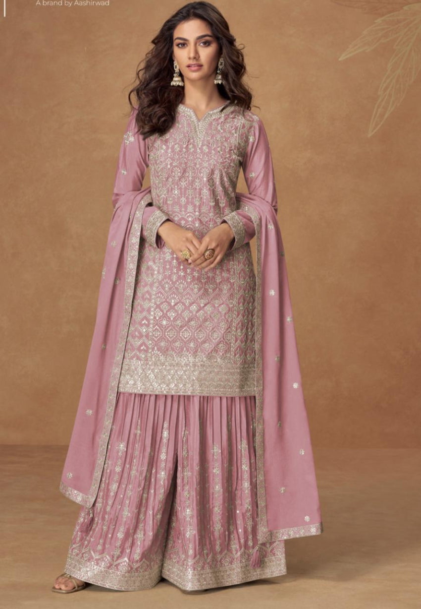 Woman wearing a pink traditional outfit with embroidery on a brown background