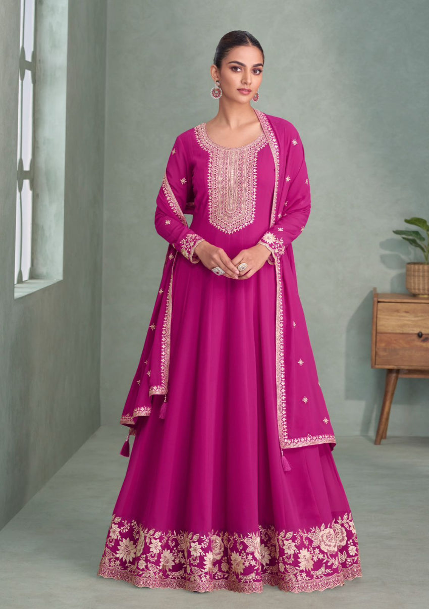 Woman wearing a pink traditional outfit with intricate embroidery in a minimalistic setting.