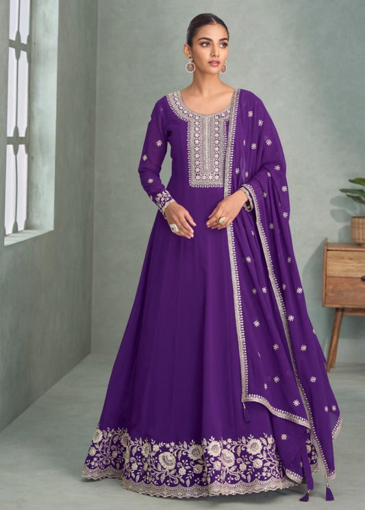 Woman wearing a purple embroidered dress with a matching dupatta in a room setting.