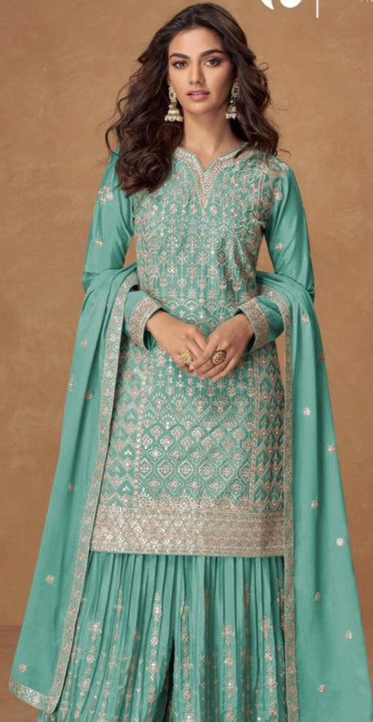 Woman wearing a teal traditional outfit with intricate patterns on a brown background