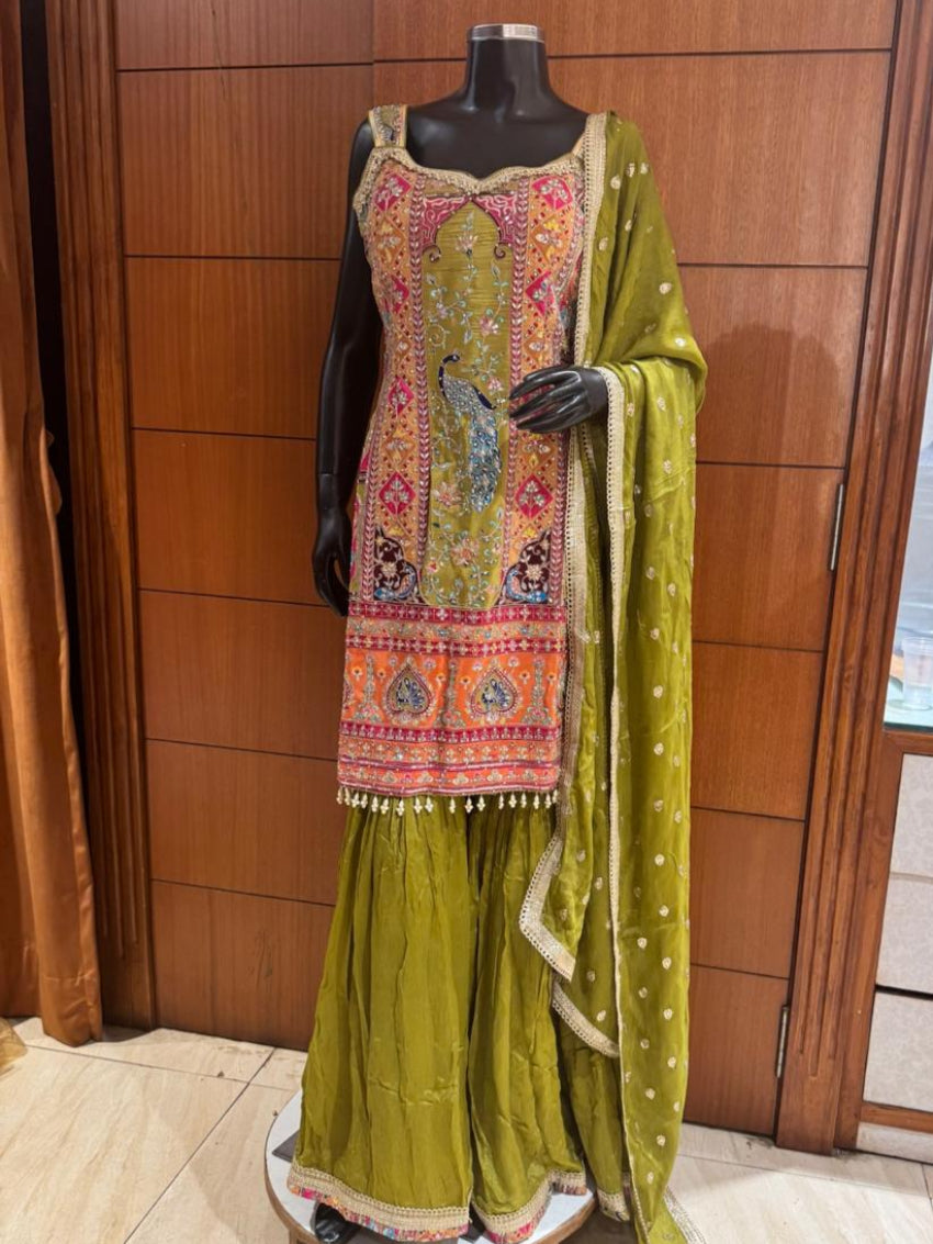 Traditional outfit with embroidered top and green skirt on a mannequin against a wooden panel background.