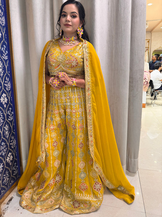 Woman in a yellow saree with floral patterns standing indoors.